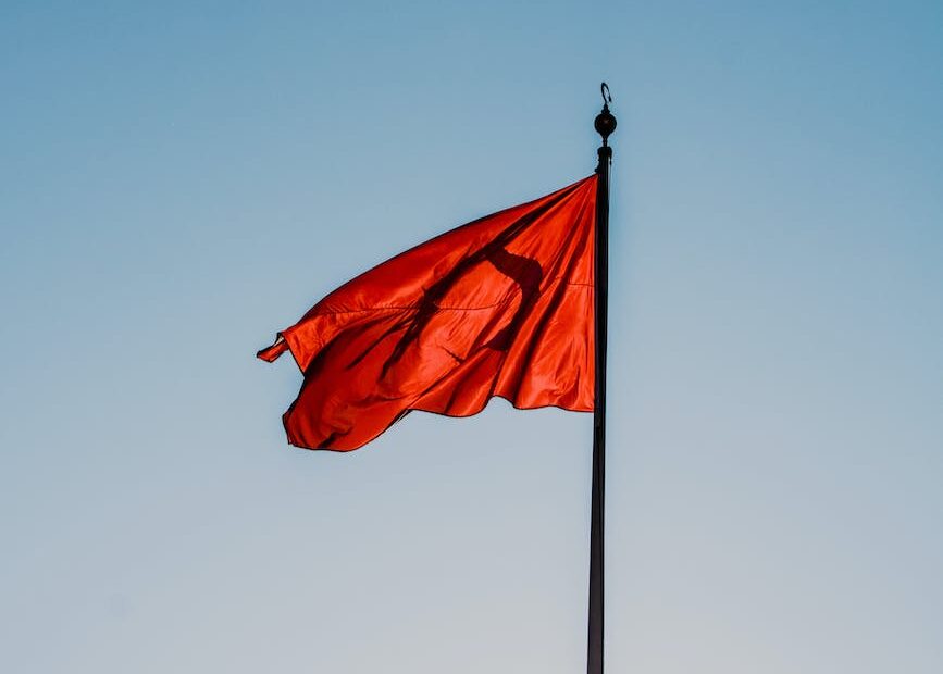 red flag on a black flagpole against blue sky