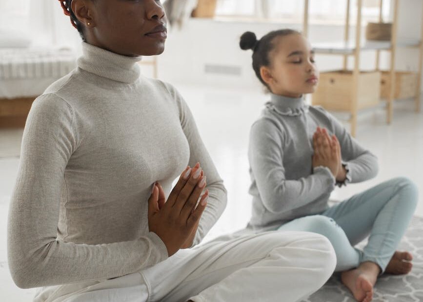 relaxed black woman with little daughter practicing lotus pose at home